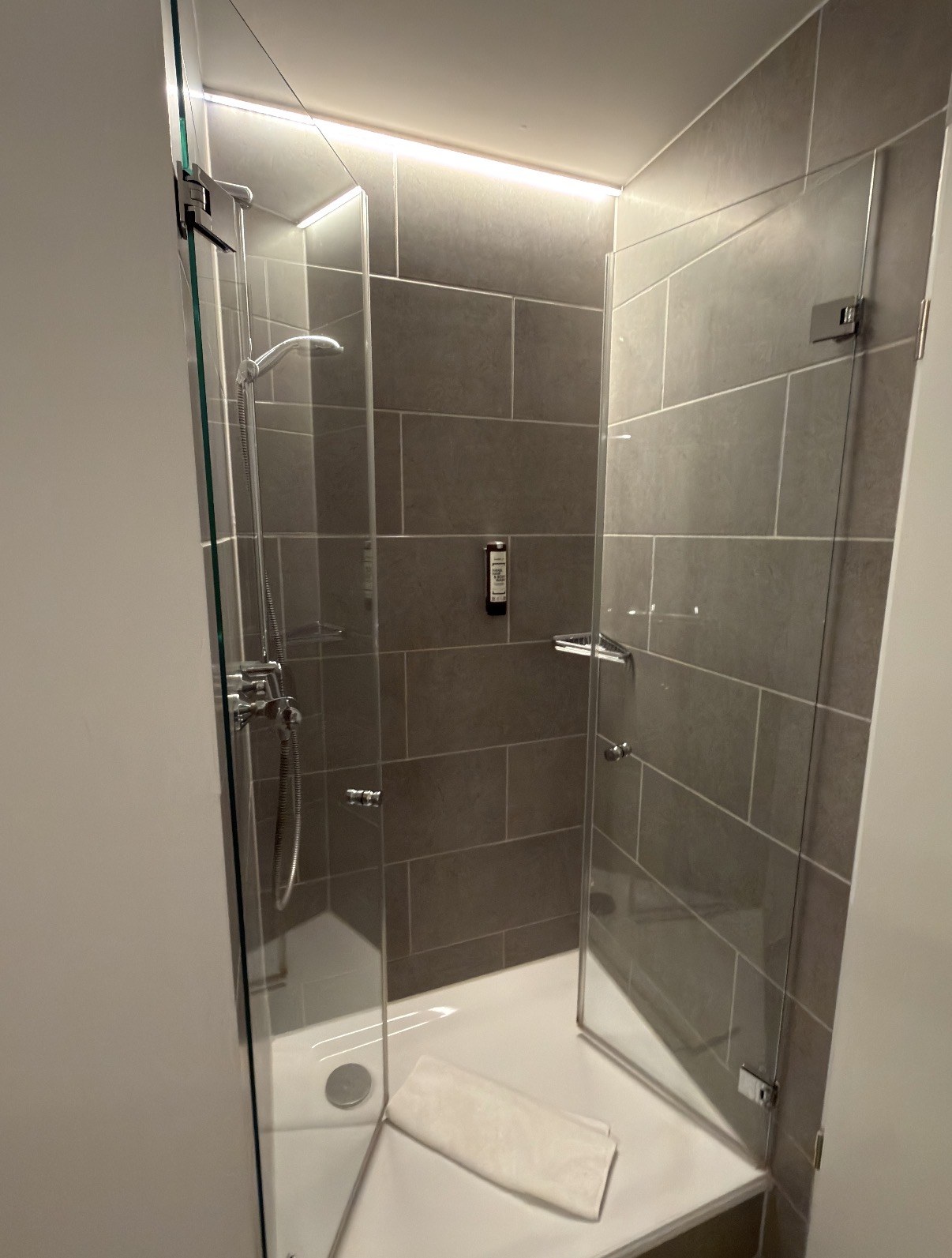 Glasdusche mit grauen Fliesen und bereitgelegtem Handtuch